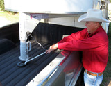 Man reaching over pickup truck bed to latch gooseneck trailer with EZE latch device