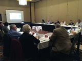 member of the NAP advisory team sit around table at meeting with projection screen in background