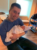 Shawn Ehlers holding his new daughter and smiling at camera
