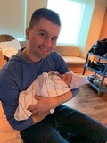 Shawn Ehlers holding his new daughter and smiling at camera
