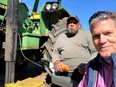 Frank Beard (back left) on John Deere tractor lift seat holding lift control in his left hand with another person on right side of picture take selfie with Frank and blue skies overhead