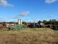Picture of farm with implements and tractors in the foreground, two silos in the background against a blue sky