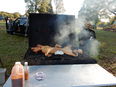 Metal table in front with jugs of sauce on it and behind that a whole hog roasting in wood-fired hog roaster