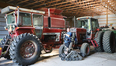 Picture of a large farm shed with a red combine and red tractor in it and in the foreground an AgrAbility client in a standing Trackchair
