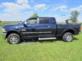 Dark blue pickup truck facing left in a green field with blue sky has silver running boards & the front one on the ground as a lift