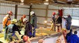 People wearing harnesses and hard hats standing in a trailer filled with grain inside a pole barn practicing rescue tube extraction.
