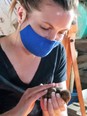 Intern Megan - a young woman with blue face mask and black v-neck T-shirt holding & petting a brown baby chick