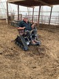 Farmer with 2 prostheses below the knee in track chair on dirt floor inside large hoop house pointing at something with left hand