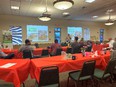Classroom with long tables covered with red table cloths. People seated in front row listening to male speaker with 2 projected images of Tennessee AgrAbility's logo and pictures of veterans 