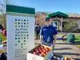 Young man in blue golf shirt standing behind table with box of apples on it & a sign to his right saying ALPHA GAMMA RHO