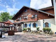 Front view of Frankenmuth Bavarian Inn - a building with stucco walls below and vertical wood siding above. Windows have curtains and blue & white shutters