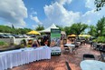 Platinum-blonde woman seated outside on patio behind long table with white table cloth & MI AgrAbility pop-up banner  beside her. Blue sky & white clouds 