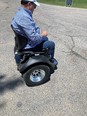 Man in white baseball cap blue long-sleeve shirt and blue jeans seated on 2-wheeled OMEO powered wheelchair