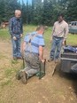 Ned Stoller & another man standing in yard while 3rd man tries out a garden kneeling bench