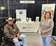 Eileen in blue jeans and gray long-sleeve top on right & farmer in cowboy hat in wheelchair on left with Tennessee AgrAbility table & pop-up banner in background