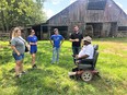 4 TSU OT students in barnyard with brown barn in background listening to African American Frank with no legs seated on motorized wheelchair