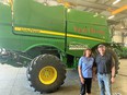Karin Rasmussen on L & Vane Clayton on Rt in front of large greeen-yellow John Deere machine with FARM RESCUE painted on side