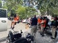 Bill Begley back to camera demonstrating truck lift to Black youths in orange shirts in parking lot with girl on lift about 4 ft off the ground