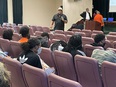 Black speaker John Jamerson in black polo shirt & straw hat speaking to youth group in auditorium at FAMU