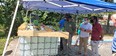 Men with face masks on standing under blue canopy looking at aquaponics demonstration
