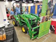 Green & yellow John Deere tractor behind green & yellow AgrAbility banner with people in background at FFA Convention