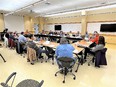 Large conference room with tables put together in a rectangle & 18 people seated around tables on outside of rectangle