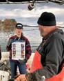 Woman & man looking at a poster on a boat with water - fall trees & cloudy skies in the background