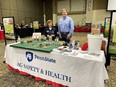 Tall man and short woman standing behind display table with white tablecloth saying PENNSTATE AG SAFETY & HEALTH in large expo room