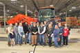 A group of people posed for picture standing in a large warehouse in front of an orange Mahindra tractor.