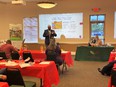 Classroom with red tablecloths on student tables - green cloth on teacher table - with PowerPoint slide on front wall - Finis Stribling teaching.