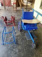 A red metal wheelchair frame & a blue walker frame & a blue wheelchair on a cement floor