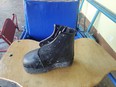 Black orthopedic leather shoe sitting on wood table with blue chair behind it