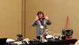 Karen Rasmussen standing behind a table & demonstrating assistive technology