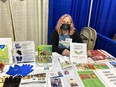Woman with face mask sitting behind table loaded with AgrAbility materials and assistive technology