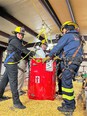 3 people in yellow helmets and rescue gear with a red grain rescue bin practicing grain bin rescue