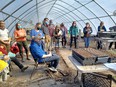Group of people standing in a hoop house looking at potted plants.