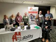 Group photo of 4 women and4 men - 1 of the men in a wheelchair - standing behind an AgrAbility of Wisconsin table.