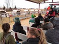 Group of people on benches in farm wagon taking tour of dairy farm with calf housing in background