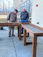 2 men outside of a building standing on cement patio looking at raised-bed garden wood tables.