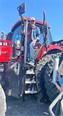 Man in blue jeans and baseball cap standing at top of ladder next to red farm tractor cab.