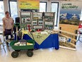 2 large Colorado AgrAbility banners in background with display table and green wagon in foreground & a woman standing facing camera on left