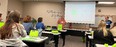 Carla Wilhite in front of classroom teaching class of rehabilitation professionals seated at desks with green KS AgrAbility bags in front of them