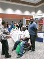 3 African American people - 2 men & a woman - talking together near a NC AgrAbility booth in a large room