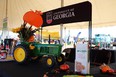 John Deere tractor sitting under a large white tent with black & red banner reading UNIVERSITY OF GEORGIA over it & AgrAbility banner in front of tractor
