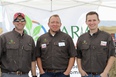 Three men all wearing brown button-down shirts with FARM AGAIN logo in front of large Farm Again banner.