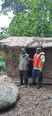 2 African men talking outside mud hut with man on right wearing orange & yellow life vest