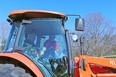 Orange Kubota tractor cab with woman in drivers seat and man in open cab doorway giving instructions