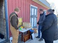 3 people looking at a table with bee & honey gear outside red barn