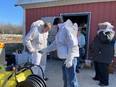 Several people in bee protective gear outside red barn on clear day