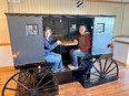 2 women - Linda Fetzer & Abbie Spackman - in mockup of Amish buggy that is a booth in a restaurant